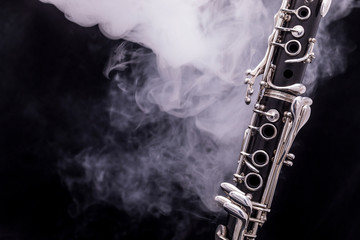 A black clarinet with silver plated keys in smoke on a black background