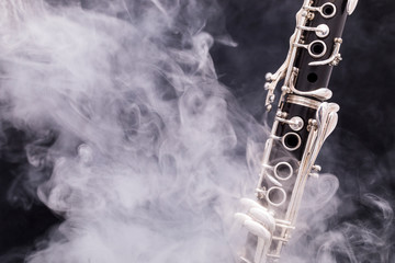 A black clarinet with silver plated keys in smoke on a black background