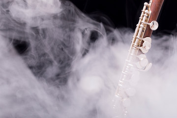 A piccolo flute from brown wood with silve plated keys in smoke on a black background