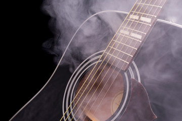 A part of a black classical guitar in smoke on a black background