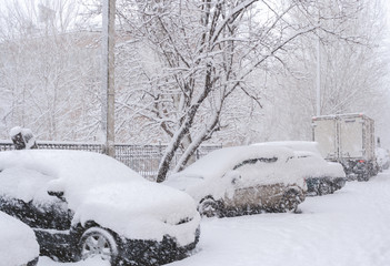 Parked snow-covered cars during plentiful snowfall in winter day.