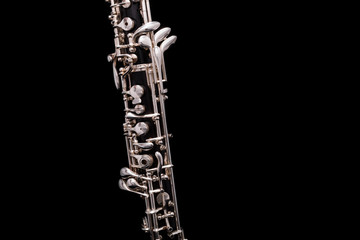 A black oboe with silver plated keys on a black background