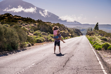 Young man and woman in relationship together walking in the middle of a long road at the mountain. barefoot man carry a nice girl on his chest and walk smiling and having fun during a day of  travel