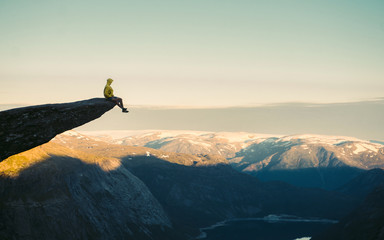 Adventurous man sitting on top of the mountain and enjoying the beautiful view during a vibrant...