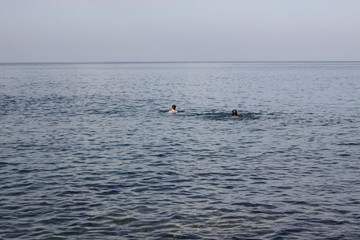 Two swimmers with faces not seen in an open see swimming to a horizon