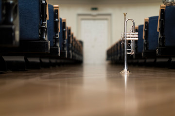A trumpet standing on its bell on the floor amongst rows of chairs