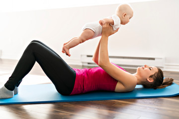 A Portrait of beautiful young mother in sports wear with her charming little baby in training...