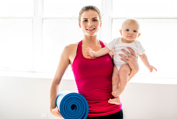 A Portrait of beautiful young mother in sports wear with her charming little baby in training session