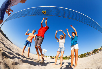 Active boys and girls playing volleyball on beach