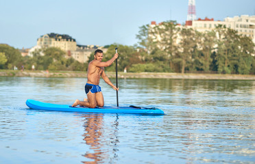 Boy on paddle board rowing in middle of city lake.