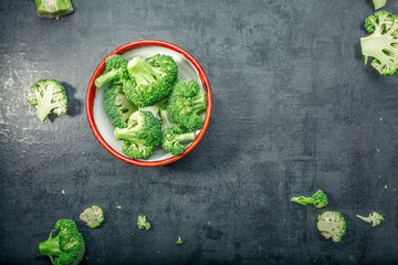 Fresh raw broccoli in a wooden bowl on a dark background.Top view. Free space.