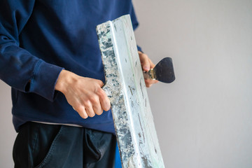 close up man holding putty knifes plastering the wall, working and repair home f
