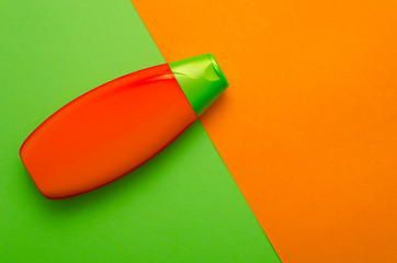 Orange and green bottle of shampoo located diagonally on the background of the same colors