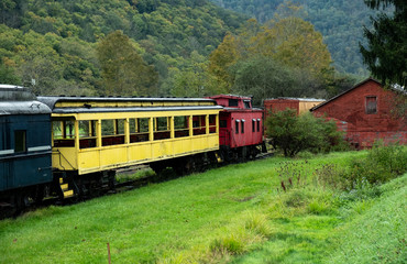 Obraz premium Colorful old rail cars sitting on the tracks in the valley below the mountians
