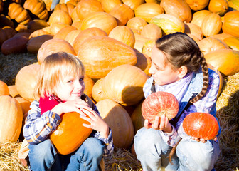 Cute Young Brother and Sister Children sitting on straw with pumkins on farm market. Family celebrating thanksgiving or halloween.