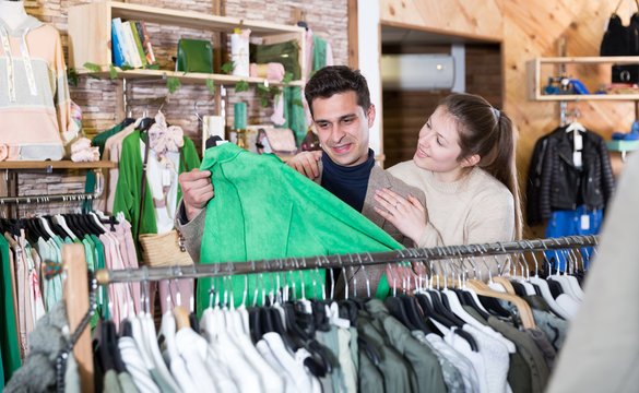 Smiling woman and man are choosing clothes and looking on green jacket