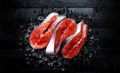 Fresh salmon steaks on black wooden background. Top view