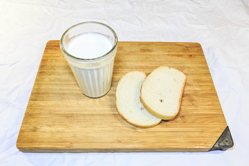 Bread cut into pieces on a wooden board next to a glass of milk
