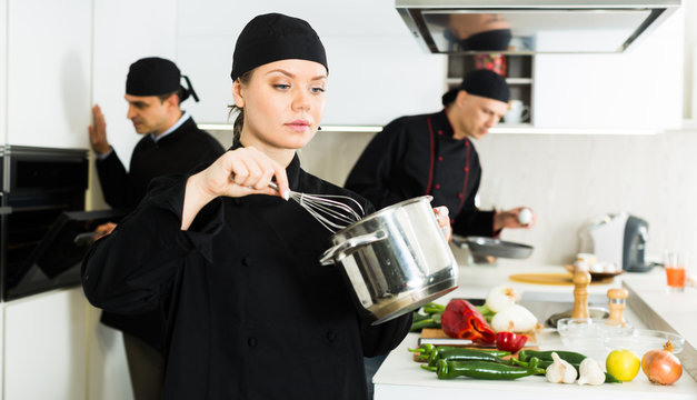 Positive female  cook with whisk, team working  on kitchen