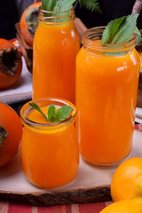 Orange smoothie topped with mint in glass jars surrounded by fruits