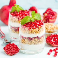 Pomegranate parfait - sweet organic layered dessert with granola flakes, yogurt and red ripe fruit seeds.