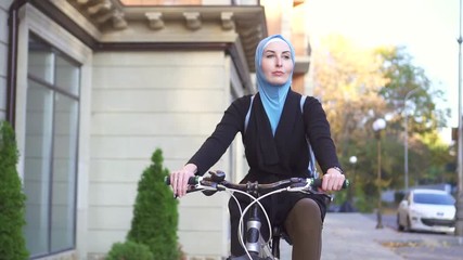 Portrait young muslim woman in a hijab on a bicycle in the city,slow mo
