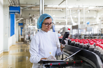 Serious middle age woman quality control worker checking robotic line for bottling and packaging carbonated black juice of soft drink into bottles.