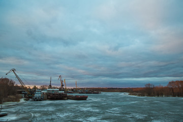 Pier with cargo ships on the frozen river.