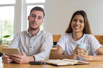 Students studying and relaxing in cafe. Young man and woman sitting at table and looking at camera. Friendship and education concept. Front view.