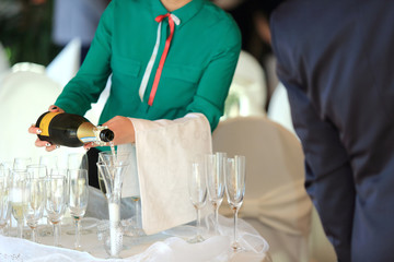 Kelnerka nalewa szampana do kieliszków na przyjęciu weselnym.