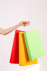 Cropped shot of female hand holding bunch of different colorful blank shopping bags over isolated white background. Many packets with in woman's arms. Black friday sale concept. Copy space, close up.