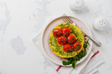 Frittata with arugula, potatoes and cherry tomatoes in iron pan on old stone table background. Top view.