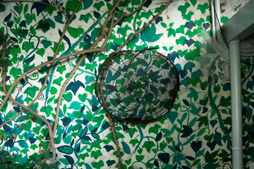 Elemento decorativo de apero de labranza antiguo en pared con hojas verdes. Ambientación vegetal con columna azul. Decoración, moderno.