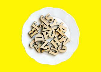Wooden letters on a white plate, yellow background