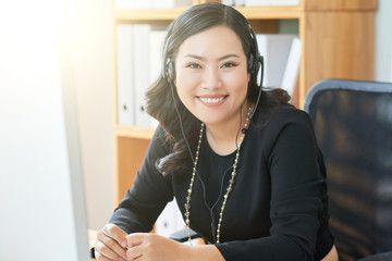 Portrait of cheerful Vietnamese business lady in headset enjoying work