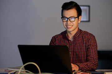 Happy Vietnamese programmer reading e-mails on laptop screen