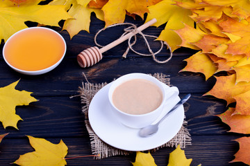 Autumn still life. Fall leaves with dark coffee with milk in a white bowl on a black table