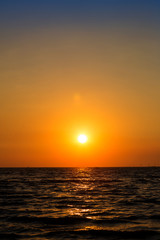 Fototapeta na wymiar Bright sunset with large yellow sun under the sea surface. Sunset over sea landscape. Beautiful sunset with sky over calm sea in tropical island