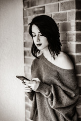 Portrait of a young caucasian woman with mobile phone on brick wall background . Image in black and white color