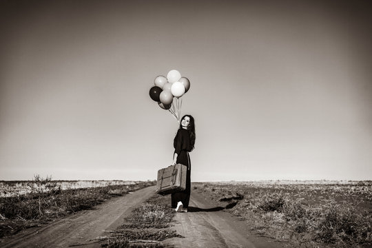 Beautiful girl in black dress with balloons on countryside . Image in black and white color