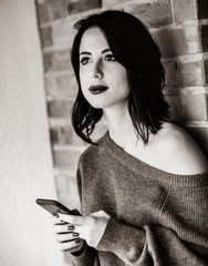 Portrait of a young caucasian woman with mobile phone on brick wall background . Image in black and white color