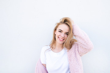 Wonderful smiling girl in a white T-shirt and a pink coat on the background of a white wall....
