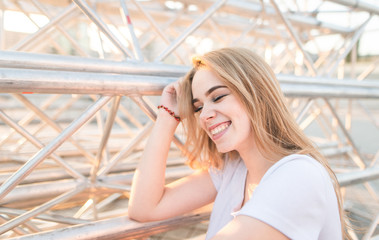 Close-up portrait of a smiling girl in white shirt with a light background. Blonde smiles sincerely with her eyes closed on a light abstract background..