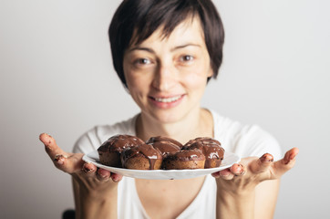 Beautiful young woman holding a plate full of homemade chocolate muffins. Selective focus.