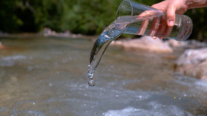 CLOSE UP: Unknown girl pours transparent liquid into the crystal clear river.