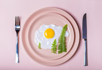 New Year's breakfast: fried eggs on beige plate. green leaves like christmas trees. a fork and a knife. view from above