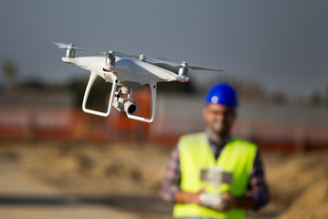 Construction worker with drone at building site - obrazy, fototapety, plakaty