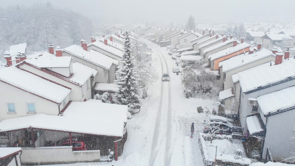 AERIAL: Car drives down the snowy road leading through the suburban neighborhood