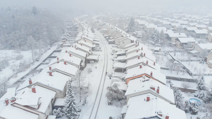 AERIAL: Flying over the empty road leading through suburbs covered in fresh snow