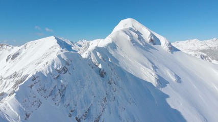Fototapeta na wymiar AERIAL: Cinematic shot of a majestic snowy mountain ridge in the sunny Alps.